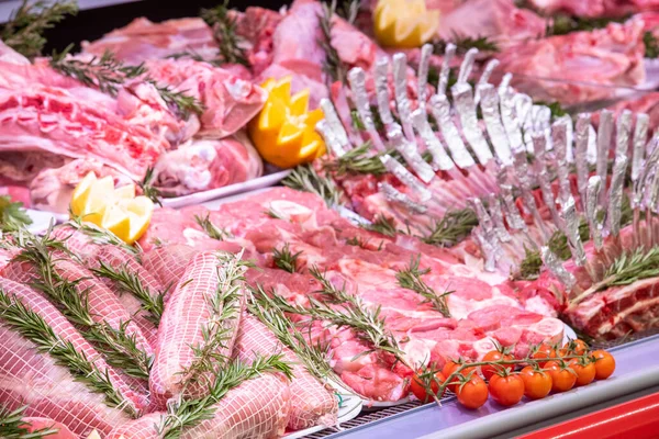 Meat department in butchery inside a mall. Various types of meat displayed in an orderly and creative way. Shelves of a food supermarket. Orange and vegetables for decoration and topping.