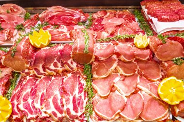 Bir alışveriş merkezinde kasaplık yapan et bölümü. Düzenli ve yaratıcı bir şekilde gösterilen çeşitli et türleri. Yiyecek süpermarketinin rafları. Süsleme ve süsleme için portakal ve sebze.