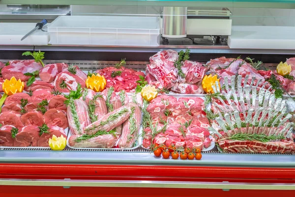 Meat department in butchery inside a mall. Various types of meat displayed in an orderly and creative way. Shelves of a food supermarket. Orange and vegetables for decoration and topping.