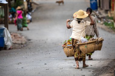 Tipik bir yöntemle yiyecek taşıyan Birmanyalı kadınlar. Karakteristik şapkalı giysiler. Sokağın solunda fotokopi odası var. Konum: Kyaukpadaung, Myanmar
