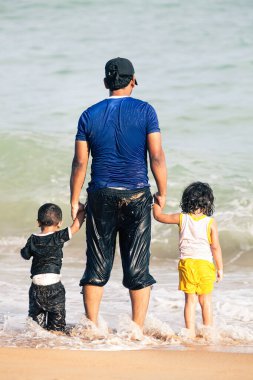 Unawatuna, Sri Lanka. 31 Temmuz 2016: Deniz kenarında el ele tutuşan iki çocuklu Arap baba. Deniz kıyısında iki küçük çocuğu olan bir baba. Denizden sırılsıklam olmuş giysiler giyiyorlar. Denize doğru bakıyorum..