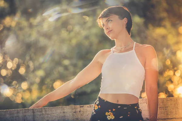 Beautiful romantic young woman with short black hair. Bright warm lights, outdoors in the city. The young woman wears a white tank top and a flowered skirt. Bokeh effect with light trails.