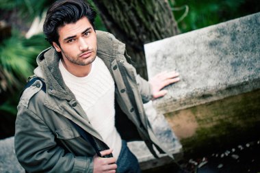 Sokakta yürüyen yakışıklı genç bir İtalyan. Yukarıdan görüldü. Şık saçlar ve açık havada kışlık ceketler, omuz çantası ve sonbahar kıyafetleri giyerek. İtalya 'da, Roma' da doğal bir parkta..