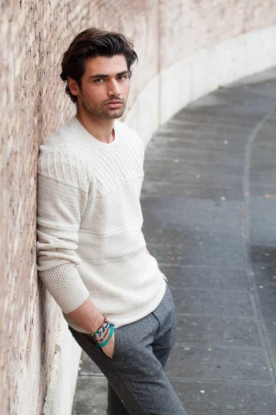 ハンサムな 深刻な若い男は長い壁の屋外で 彼のポケットに手にもたれている カジュアルな服 冬のスタイル 白いセーター 通りの街で — ストック写真