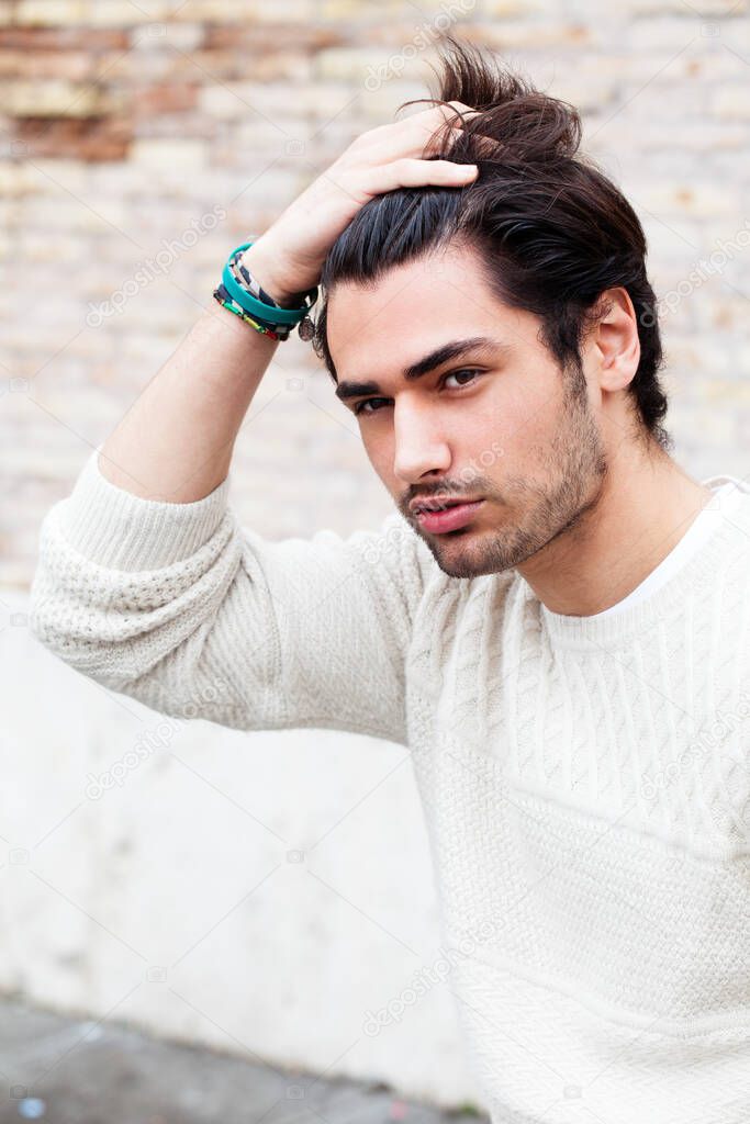 Young handsome man passing his hand through his hair. Trendy hair and stubble beard. Serious attitude. White sweater.