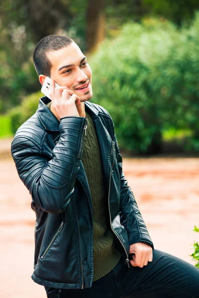 スマートフォンを持っている幸せな若い男 電話で話してる 若いハンサムな男が誰かと電話で話している 彼の気分は肯定的だ 公園の屋外 — ストック写真