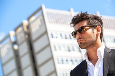Harika bir stil adamı. Güneş gözlüğü. Şehir tarzı. Dışarıda güneş gözlüklü, güzel ve çekici bir adam. Kirli sakal ve siyah saç. Yoğun ışık. Beyaz gömlek ve şık ceket..