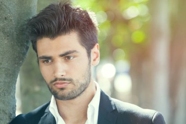 Genç ve yakışıklı bir adamın endişeleri ve düşünceleri. Güzel ve şehvetli bir adam düşünceli, bir ağacın yanında. Bakış, sakal ve şık saçlar..