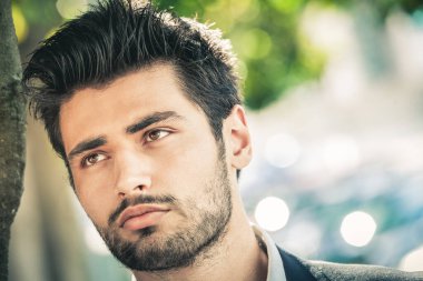 Güzel ve çekici bir adamın yakın plan portresi sakallı, şık saçlı, parlak gözlü ve rüya gibi bir yüz ifadesi olan. Gün ışığında dışarıda..