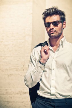 Dışarıdaki yakışıklı seksi adam. Zarif ve şehvetli. Güneş gözlüğü. Zarafet ve güzellik. Açık havada. Genç adam beyaz bir gömlek giyiyor..