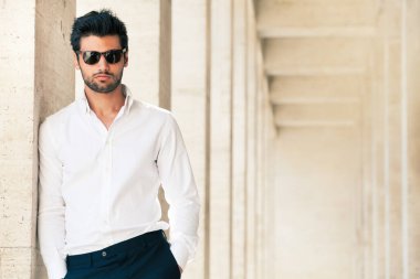 Güneş gözlüklü çekici ve şık bir genç. Dışarıda mermer duvara yaslanmış..