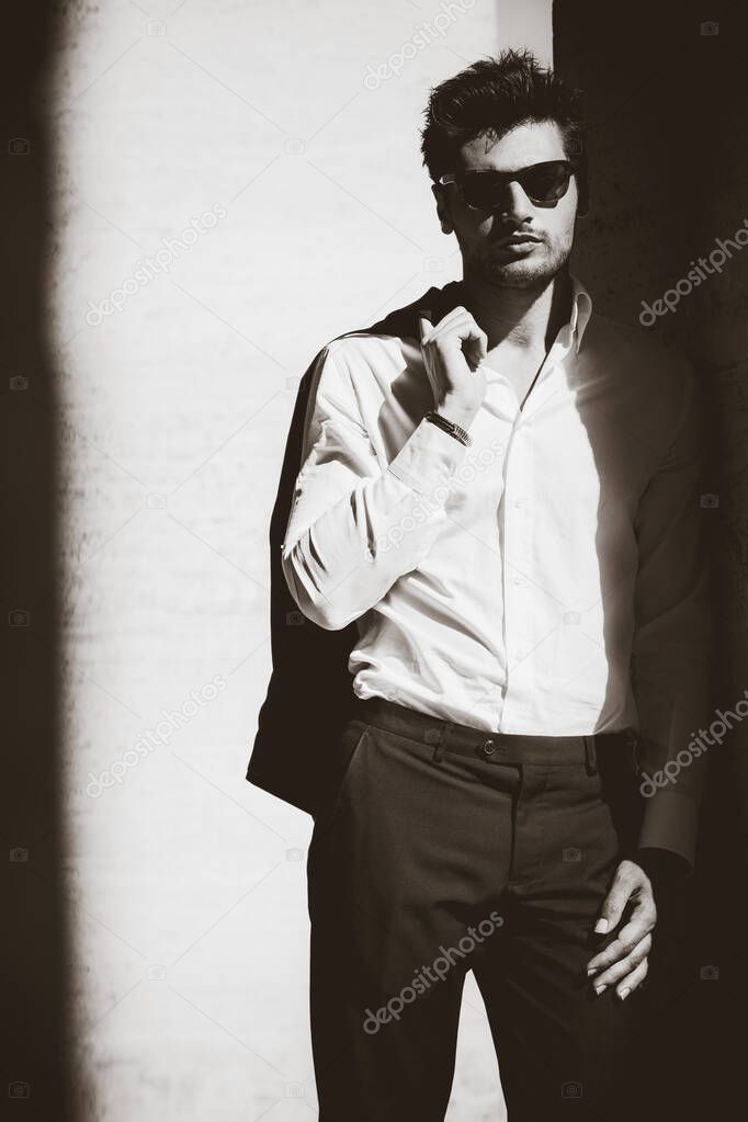 Cool man with sunglasses and white shirt. In twilight leaning against the wall. Black and white with shades.