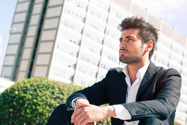 Handsome man model sitting watching. Career and job opportunities. Young entrepreneur, behind him a building with offices.