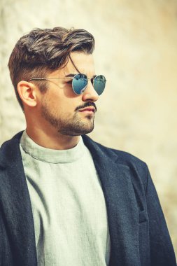 Güneş gözlüklü, modern saç stili ve sakallı yakışıklı bir adam. Dışarıda, sokakta. Beyaz tişört ve siyah ceket..