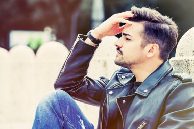 Endişeli genç adam, endişeli konsept. Genç, güzel ve modern bir adam alnıyla oturuyor. Düşünceli ve biraz endişeli. Dışarıda, parkta..