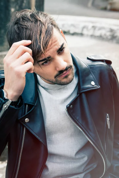 若いハンサムな男は ストレートの茶色の髪に触れる屋外 チャーミングで若々しい表情 革のジャケットと薄い髭 — ストック写真