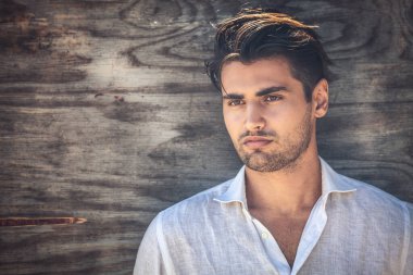 Erkek portresi, tahta arka planda genç ve yakışıklı bir adam. Beyaz bir gömlek giyiyor ve açık renk bir sakalı var..