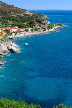 Sahili, kayaları ve İtalya 'daki Elba Adası' nın kayalık yamacıyla. Sahilde güneşlenen bir sürü insan var. Hava manzaralı mavi deniz. Küçük bir köyün konutları.