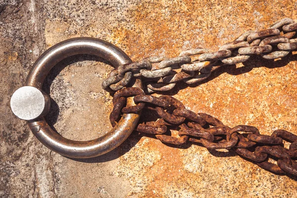 Rusty steel ring and mooring lines in a seaport. Rusty iron chain on the concrete ground.