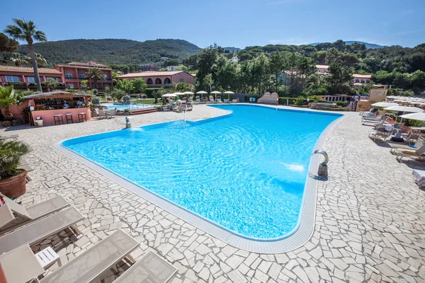 Outdoor Swimming Pool. A swimming pool and outdoor spa with poolside. Hills and green trees in the distance. Location: Procchio, Elba Island. Italy.