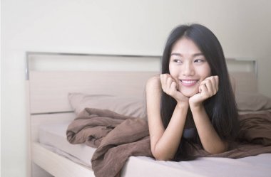 Güzel genç Asyalı kadın yatakta döşeme çekici gülümseme ile
