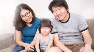 Asya Aile kanepede oturan ve kameraya bakıyor 