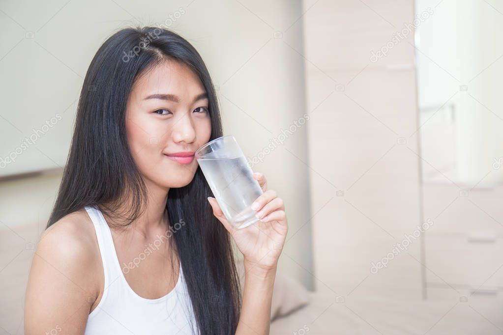 Woman drinking water from glass in modern light bedroom 