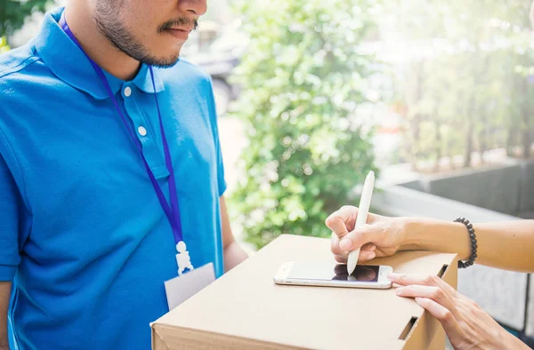 Kvinna tillägger signera signatur efter att acceptera en leverans av lådor från deliveryman, ta emot och leverans koncept — Stockfoto