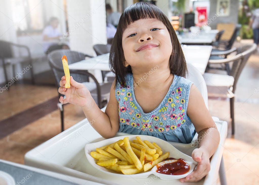 Portrait of little asian girl eating french fries in fast food restaurant close up