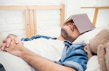 Genç Asyalı adam yüz kitap ile yatakta yalan denim giysileri 