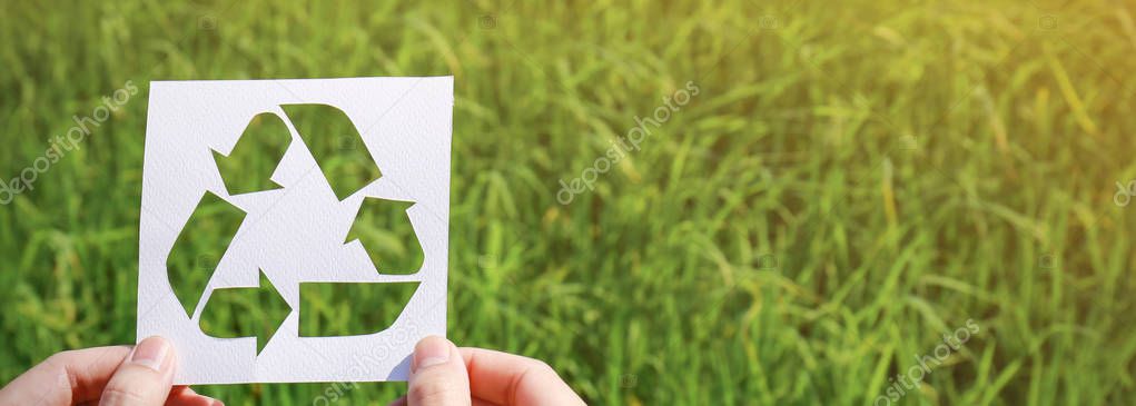 hands holding cut paper with logo of recycling over green grass background