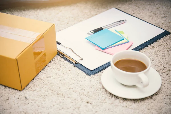 white cup with coffee, box, sheets of paper with handle on carpet