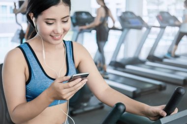 Güzel Asyalı kadın smartphone vasıl jimnastik salonu üzerinden müzik dinleme