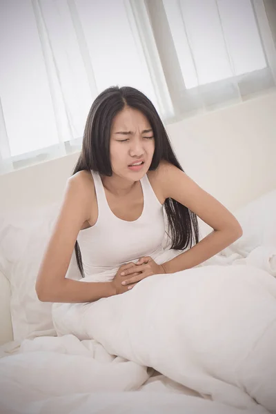 young woman with stomach ache touching tummy hands in bedroom