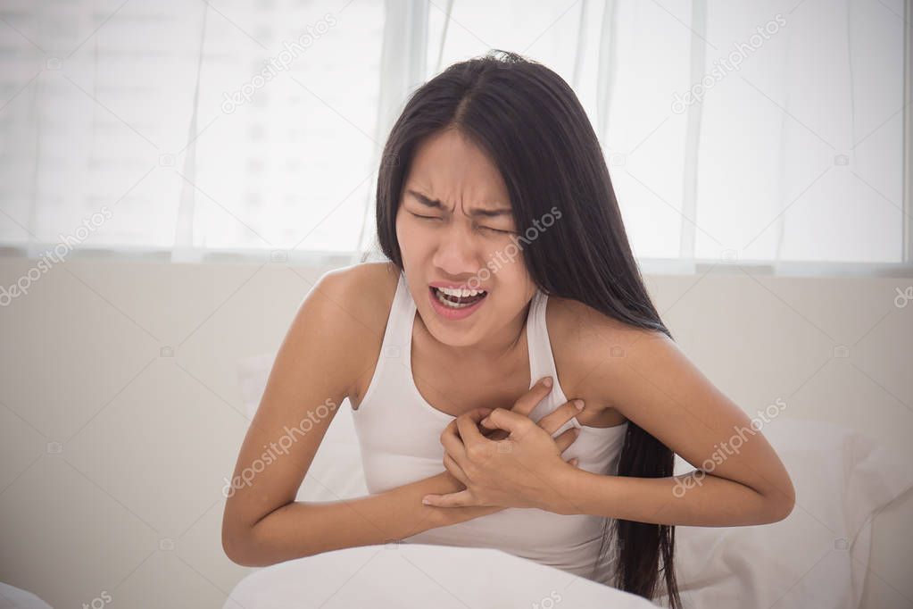 Young woman in sleepwear having heart attack in bedroom 