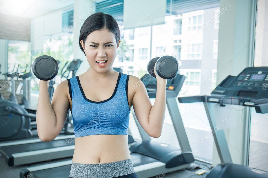 Sport asian woman holding dumbbells and training hard in gym