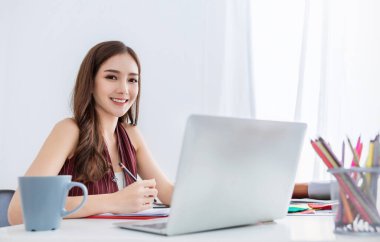 Ofis masasında bilgisayar kullanarak çalışan gülümseyen Asyalı güzel bir iş kadını portresi. Küçük işletme çalışanları serbest internet pazarlama e-pazarlama konsepti