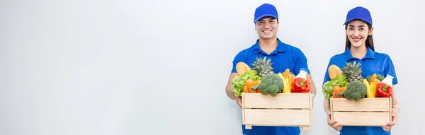 亚洲夫妇送货员身穿蓝色制服 头戴木篮 食品杂货新鲜蔬菜 与白色隔离的服装肖像 健康的生活方式网上购物网上超市投递团队合作 图库图片