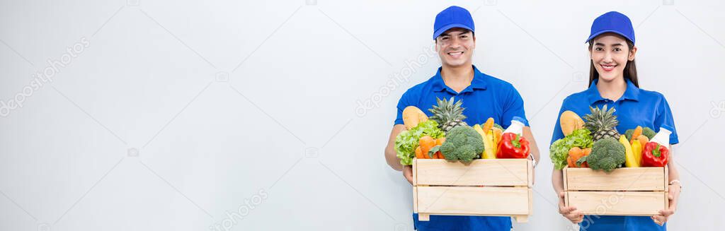 Closeup portrait of asian couple delivery man woman in blue uniform holdwood basket of grocery fresh vegetables food isolated on white. Healthy lifestyle shopping internet online supermarket delivery teamwork