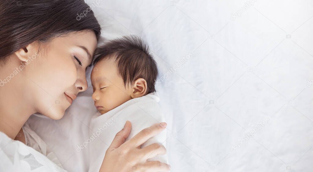 Close up portrait of beautiful young asian or caucasian mother girl kissing her healthy newborn baby sleep in bed with copy space. Healthcare and medical love asia woman lifestyle mother's day concept