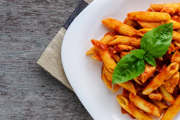 Domates sosu ve ahşap arka plan üzerinde fesleğen ile Penne