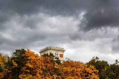 Gökyüzünde yaklaşan bir fırtına karşı bir saat ile uzun bir bina. Yaprakları ve yaklaşan fırtına arasında eski bir bina