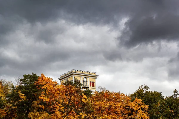 Gökyüzünde yaklaşan bir fırtına karşı bir saat ile uzun bir bina. Yaprakları ve yaklaşan fırtına arasında eski bir bina