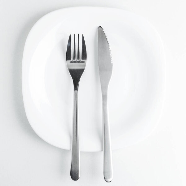 cutlery, fork and knife on an empty white plate on a white background. Table etiquette, finished