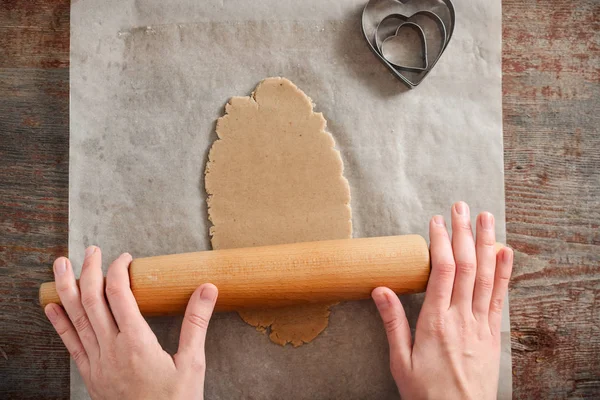 woman rolls the dough with a rolling pin on a wooden table.