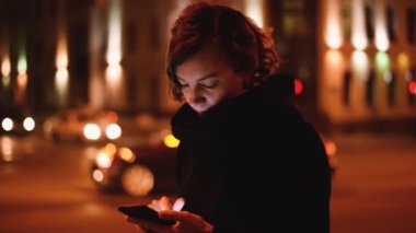 Gece şehrinde cep telefonu kullanan bir kadın. Dikkati dağılmış sokak lambalarına karşı akıllı telefon tutan kadınların ellerini kapatın.