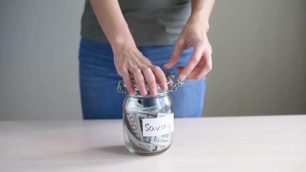 Woman Putting Paper Dollar Bill Glass Piggy Bank Inscription Saving — Stock Video