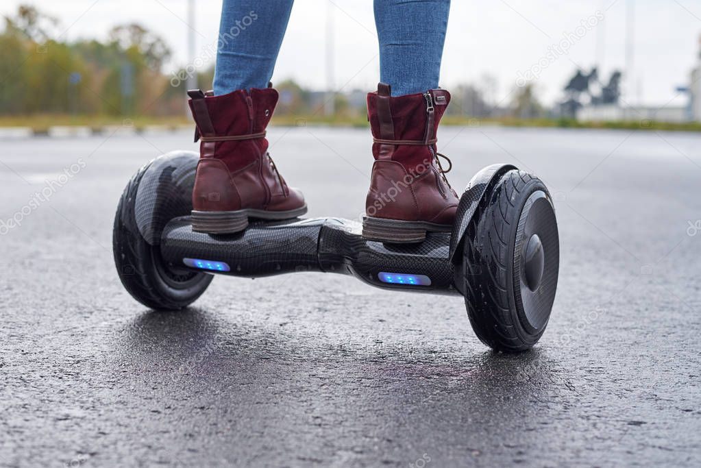 Close up of woman using hoverboard on asphalt road. Feet on elec