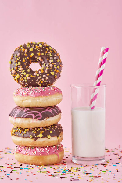 colorful donuts glazes with sprinkles and glass of milk on a pink background