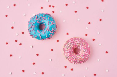 İki donut süsleme, serpiştirme ve pembe arka planda kalp şeklinde konfeti.